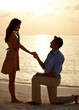 Man proposing marriage to surprised woman at beach sunset