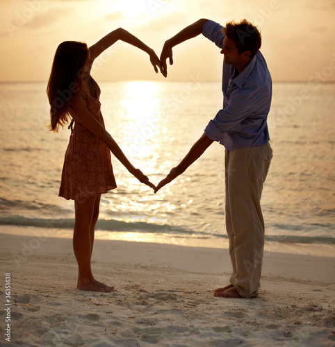 Photo: Romantic couple making heart shape with arms on beach at sunset Romantic couple making heart shape with arms on beach at sunset