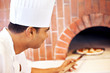 Chef putting pizza in wood fire oven in restaurant Chef putting pizza in wood fire oven in restaurant