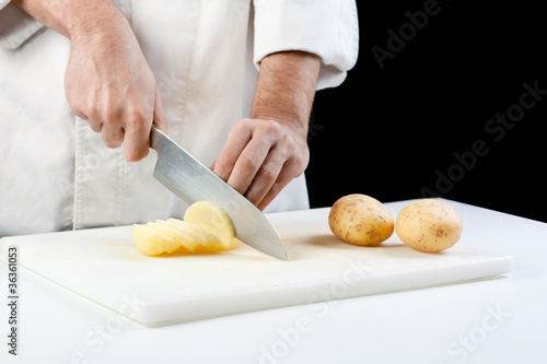 Photo: Chef cutting potatoes on black background Chef cutting potatoes on black background