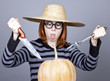 Funny girl in cap and fork with knife try to eat a pumpkin.