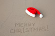 Photo: Merry Christmas written on the sand beach under red Santa hat Merry Christmas written on the sand beach under red Santa hat