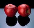 Two red apples with water drops on a dark reflection.