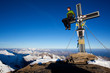 Young man sitting on a summit cross in the Alps