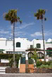 Entrance to two houses with palm trees and blue sky with clouds