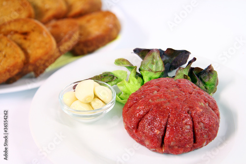 Photo: Steak tartare with garlic on white plate with onions and toast Steak tartare with garlic on white plate with onions and toast