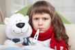 Little sick girl with thermometer embraces toy bear in bed