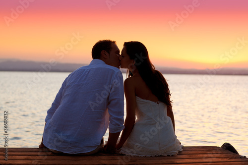 Foto: couple kissing at sunset sitting in jetty couple kissing at sunset sitting in jetty