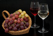 Foto: Cesto con uva e calici di vino su sfondo nero Cesto con uva e calici di vino su sfondo nero