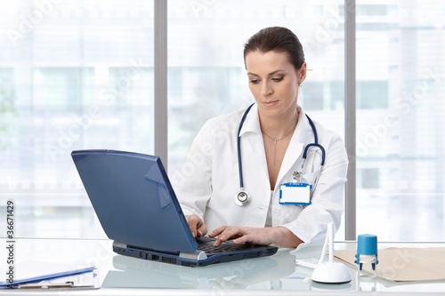 Photo: Female doctor sitting at table with laptop Female doctor sitting at table with laptop