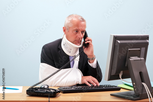 Photo: Injured businessman at his desk on the phone Injured businessman at his desk on the phone