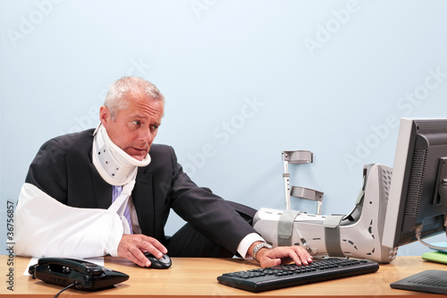 Photo: Injured businessman working at his desk Injured businessman working at his desk