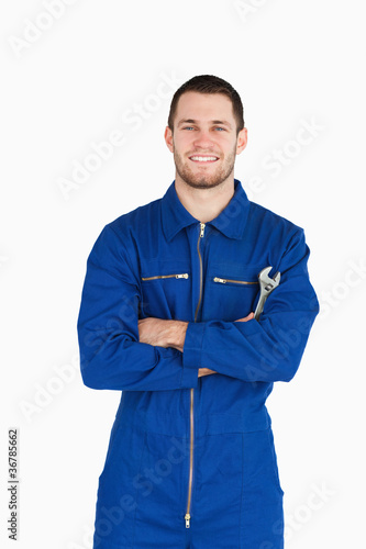 Photo: Smiling young mechanic in boiler suit with wrench and arms folde Smiling young mechanic in boiler suit with wrench and arms folde