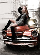 Young beautiful girl sitting on top of red retro car
