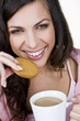 A young woman holding a cup of tea, eating a biscuit