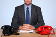 Businessman sat at desk with two telephones.