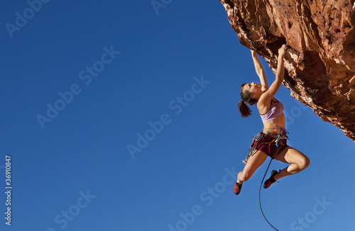 Photo: Female climber clinging to a cliff. Female climber clinging to a cliff.