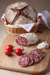 Slices salami on board, cherry tomatoes bread in breadbasket