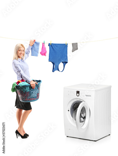 Foto: Young woman hanging clothes on clothes line next to a washing ma Young woman hanging clothes on clothes line next to a washing ma