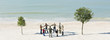 Group of people holding hands in circle between two trees on beach