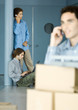 Male colleagues using laptop and cell phone, cardboard boxes in foreground