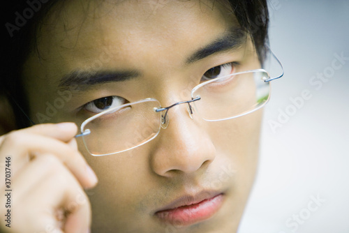 Photo: Man adjusting glasses, looking at camera, close-up Man adjusting glasses, looking at camera, close-up