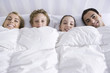 Family lying together in bed beneath comforter, smiling at camera