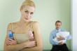 Woman holding baby bottles, smiling at camera, husband holding baby in background