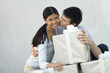 Couple standing behind stack of large gift boxes, man kissing woman on cheek