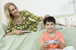 Young boy sitting on floor playing video game, mother relaxing on sofa
