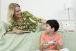 Young boy sitting on floor playing video game looking up at mother relaxing on sofa