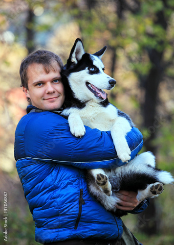 Photo: Portrait of young man holding his husky dog outdoors Portrait of young man holding his husky dog outdoors