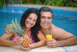 Pareja hispana en una piscina comiendo frutas.