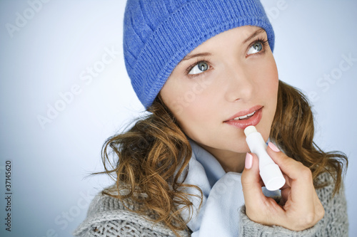 Photo: A young woman applying lip balm, in wintertime A young woman applying lip balm, in wintertime