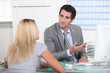 Suited man talking to a young woman across a desk