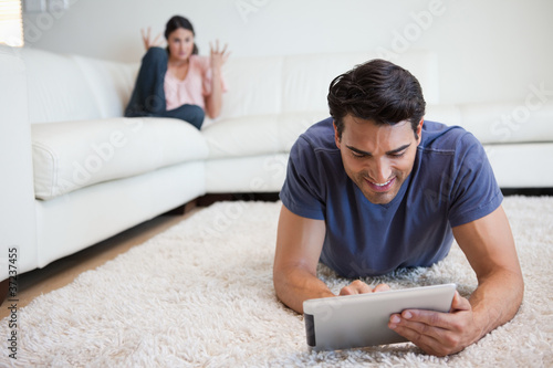 Photo: Man using a tablet computer while his girlfriend is getting mad Man using a tablet computer while his girlfriend is getting mad