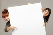 Two women peeking over edge of blank banner