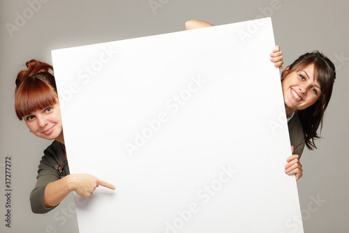 Photo: Two women peeking over edge of blank banner Two women peeking over edge of blank banner