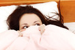 Scared woman hiding her face under the sheet.