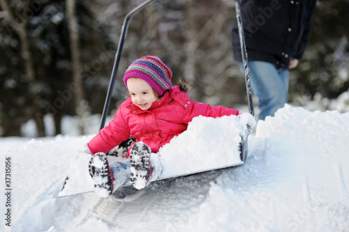 Photo: Winter fun: little girl having a ride on a snow shovel Winter fun: little girl having a ride on a snow shovel