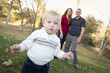Cute Young Boy Walking as Parents Look On From Behind