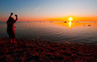 A boy jumping and throwing stones in water at sunset