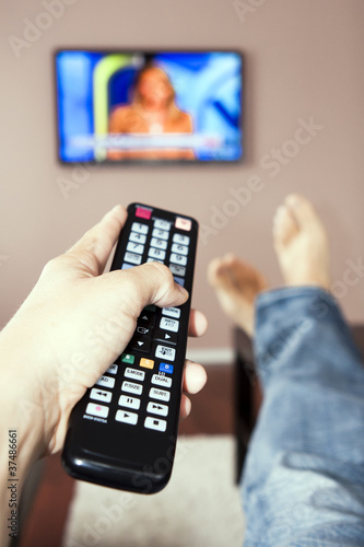 Photo: Young man watching the television, the remote control in hand. Young man watching the television, the remote control in hand.