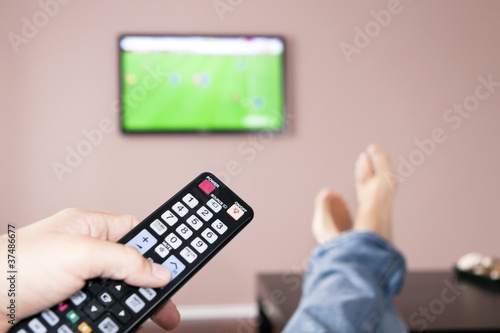 Photo: Young man watching the television, the remote control in hand. Young man watching the television, the remote control in hand.