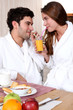 young couple in bathrobe drinking orange juice out of straw