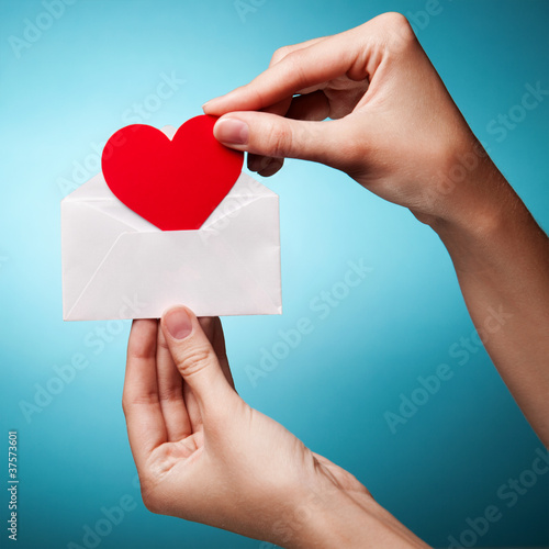 Photo: woman's hand holding an envelope with a sign of the heart agains woman's hand holding an envelope with a sign of the heart agains