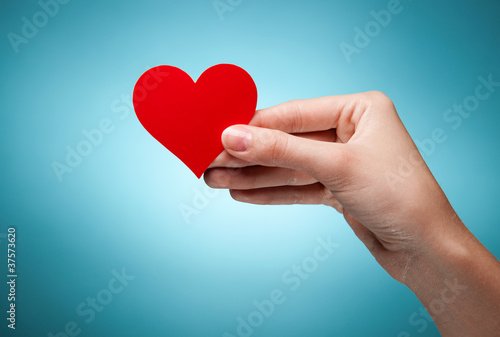 Photo: woman's hand holding symbol - red heart. Against blue background woman's hand holding symbol - red heart. Against blue background