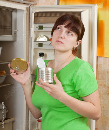 Photo: woman putting with metal can near fridge woman putting with metal can near fridge