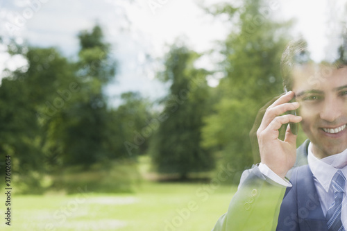 Photo: Businessman standing behind glass talking on cell phone Businessman standing behind glass talking on cell phone