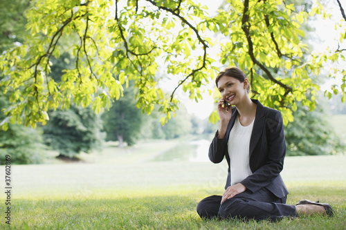 Foto: Businesswoman sitting in grass talking on cell phone Businesswoman sitting in grass talking on cell phone
